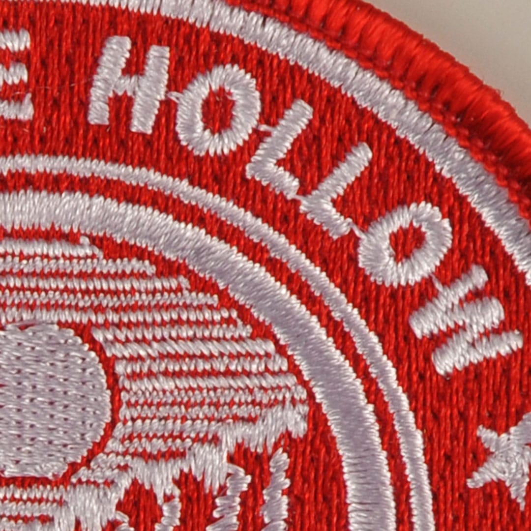 Close-up of an embroidered patch highlighting jump stitches, with visible text and a detailed design in red and white threads