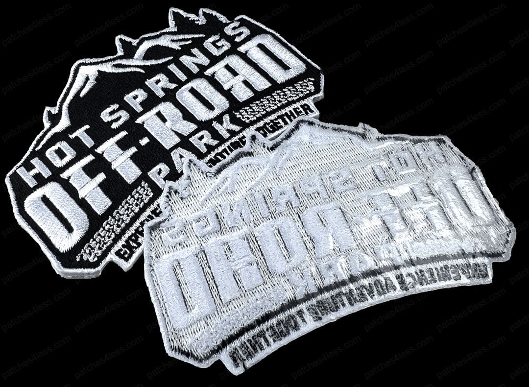Two patches for Hot Springs Off-Road Park. One is black with white text and mountain imagery, and the other is a silver version with the same design. Both patches read 'Hot Springs Off-Road Park' and 'Experience Everything Together'.
