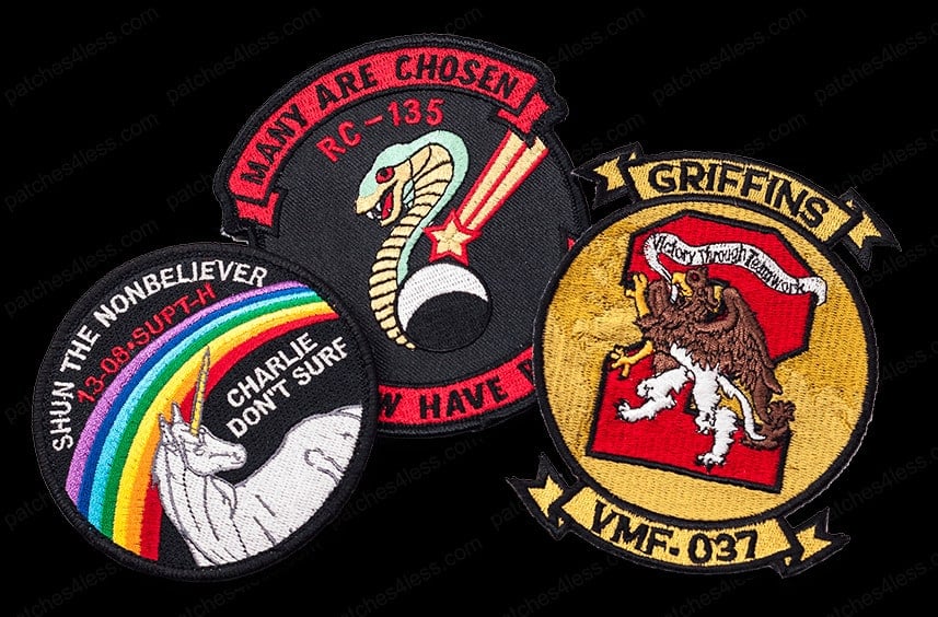 Three morale patches. One features a unicorn with a rainbow and the text 'Shun the Nonbeliever 13.08-SUPT-H Charlie Don't Surf', another has a cobra and the text 'Many Are Chosen RC-135 Few Have', and the third shows a griffin with the text 'Griffins VMF-037 Victory Through Dedication'.