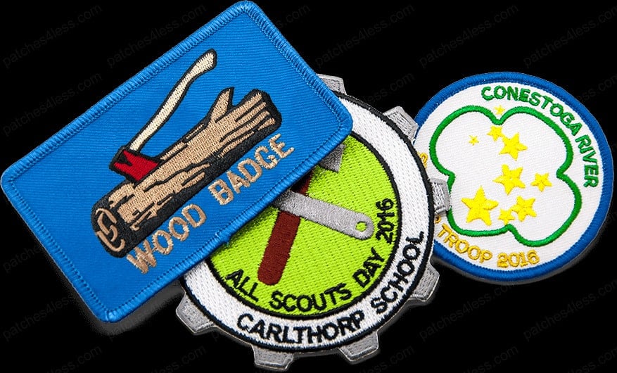 Three scout patches. One is a rectangular patch with a log and axe and the text 'Wood Badge', another is a gear-shaped patch with the text 'All Scouts Day 2016 Carlhthorp School', and the third is a circular patch with stars and the text 'Conestoga River Troop 2016'.