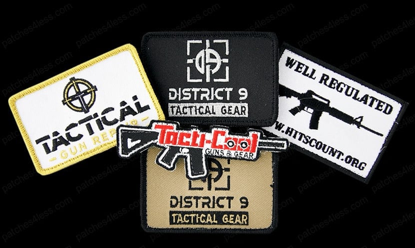 Five tactical gear patches. One reads 'Tactical Gun Report' with a crosshair design, two read 'District 9 Tactical Gear' with one in black and the other in tan, another says 'Well Regulated' with a rifle image, and the last is 'Tacti-Cool Guns & Gear' with a rifle illustration.
